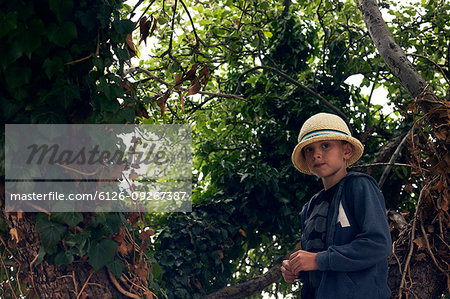 Boy wearing sun hat amongst tree branches