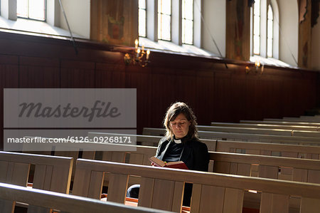 Priest reading bible on church pew