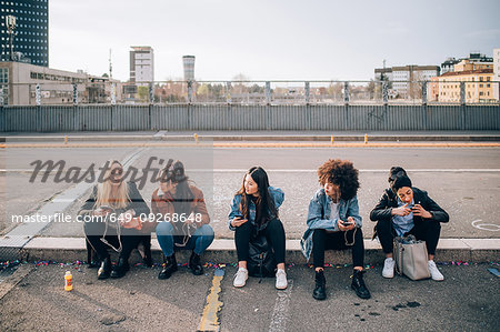 Friends sitting on kerb using smartphone, Milan, Italy