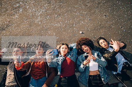 Friends together on kerb taking selfie and using smartphones, Milan, Italy