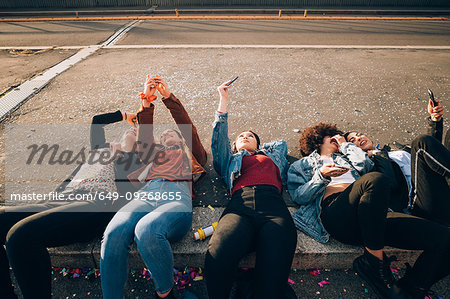 Friends together on kerb taking selfie and using smartphones, Milan, Italy