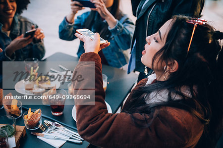 Friends taking photos of their food and drinks at outdoor cafe, Milan, Italy