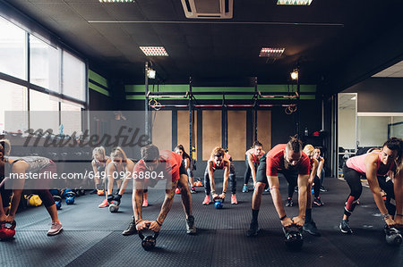 Women training in gym with male trainers, preparing to lift kettle bells