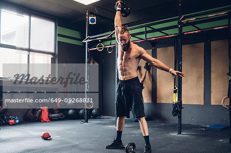 Young man training in gym, lifting kettle bell