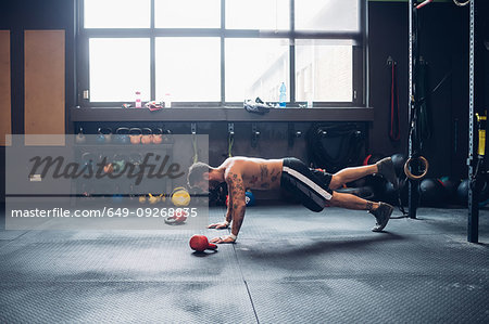 Young tattooed man training in gym, doing push ups on floor