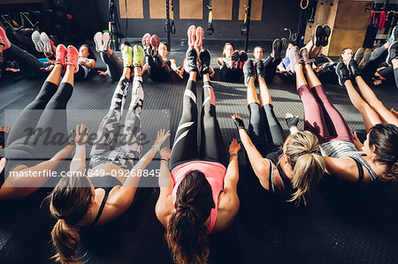 Large group of women training in gym, sitting on floor with legs raised