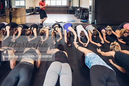 Large group of women training in gym with male trainer, doing push ups