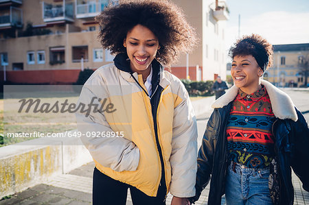 Two young female friends strolling on urban sidewalk