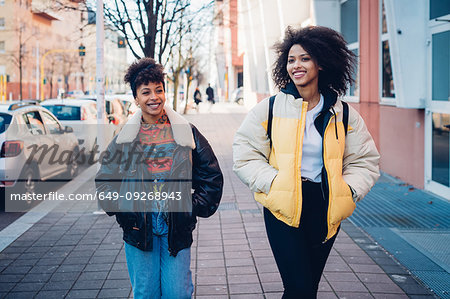 Two cool young women strolling on urban sidewalk