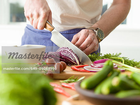 Man slicing red cabbage at kitchen counter, mid section