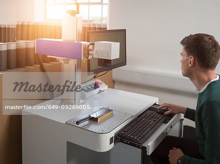 Knife factory worker using computer keyboard to operate laser cutting equipment in workshop