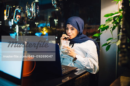 Young woman in hijab drinking smoothie in cafe