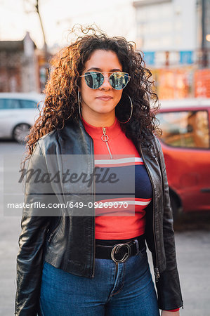 Mid adult woman with long curly hair wearing shades on city sidewalk, portrait