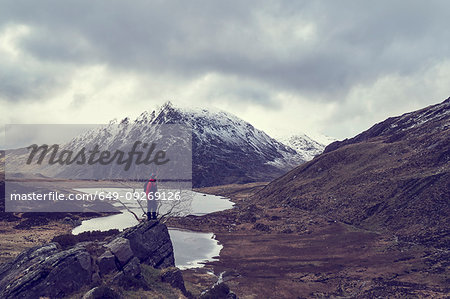 Male hiker looking out at lake and snow capped mountain landscape, Llanberis, Gwynedd, Wales