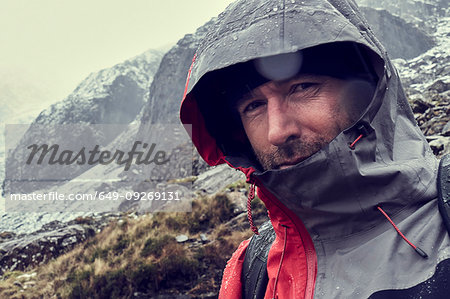 Male hiker with hood up in sleeting snow capped mountain landscape, close up portrait, Llanberis, Gwynedd, Wales