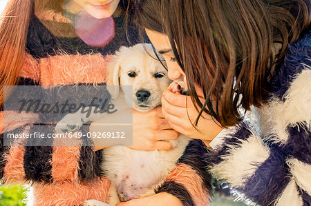 Two girl petting a cute golden retriever puppy, cropped