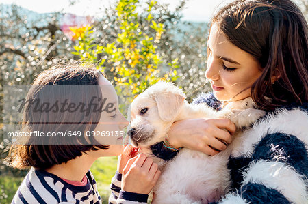 Two girls holding and petting a cute golden retriever puppy in orchard, Scandicci, Tuscany, Italy