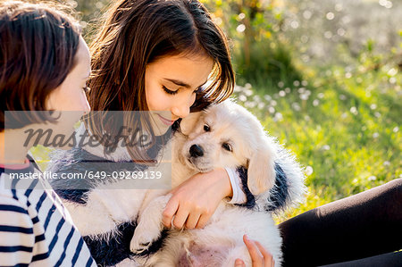 Two girls sitting in orchard hugging a cute golden retriever puppy, Scandicci, Tuscany, Italy