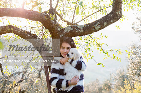 Girl holding a cute golden retriever puppy on tree ladder in sunlit orchard, portrait, Scandicci, Tuscany, Italy