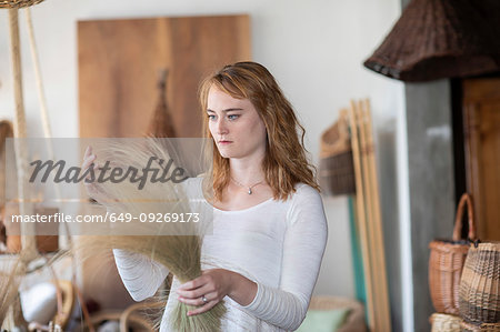 Young female basket maker examining dried grasses in workshop