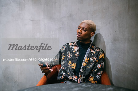 Stylish man using cellphone, concrete wall background