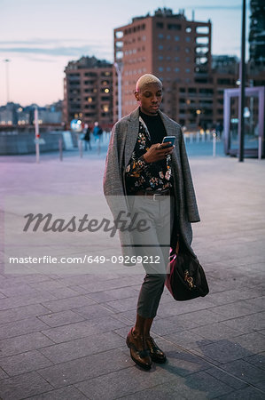 Stylish man walking through piazza using cellphone, Milan, Italy