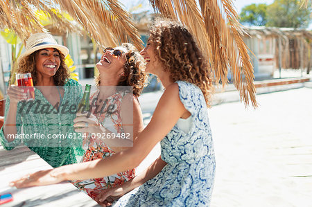 Happy women friends drinking at sunny beach bar