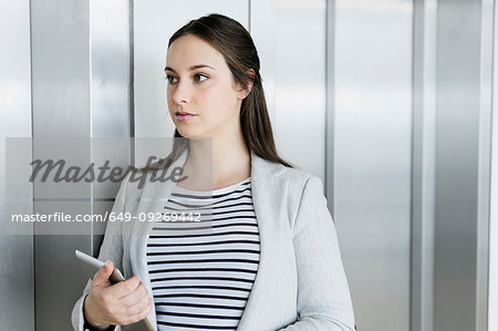 Businesswoman with digital tablet leaning against elevator door