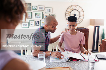 Father helping teenage son with homework in kitchen