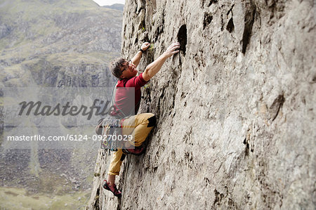 Focused male rock climber scaling rock face