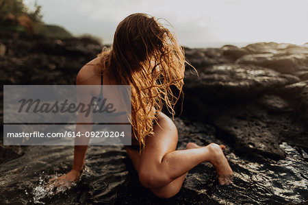 Woman posing on rocks by sea, Princeville, Hawaii, US