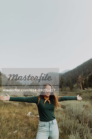 Young woman standing with open arms in rural valley, Mineral King, California, USA