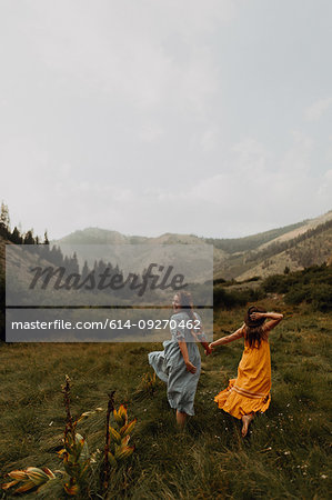 Two women holding hands running in rural valley, rear view, Mineral King, California, USA