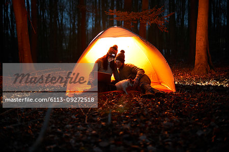 Couple using digital tablet inside glowing tent in woods at night