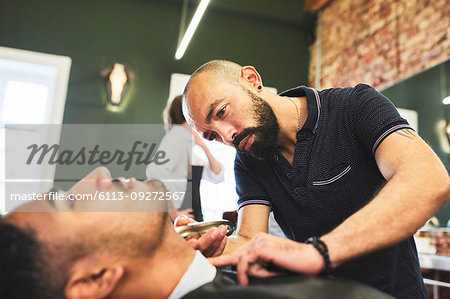 Focused male barber giving customer a shave in barbershop