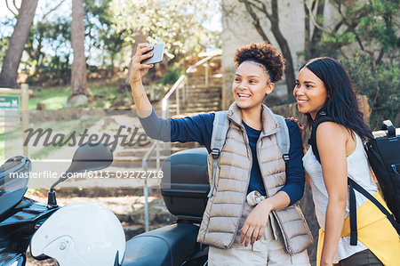 Happy young women friends taking selfie with camera phone at motor scooter