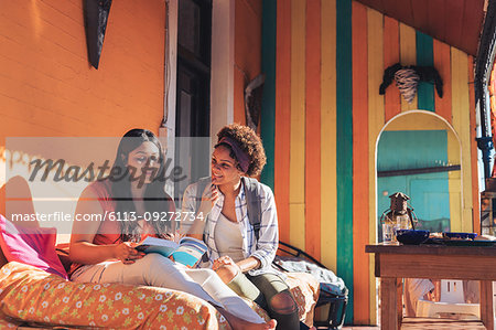 Young women friends reading book on sunny patio