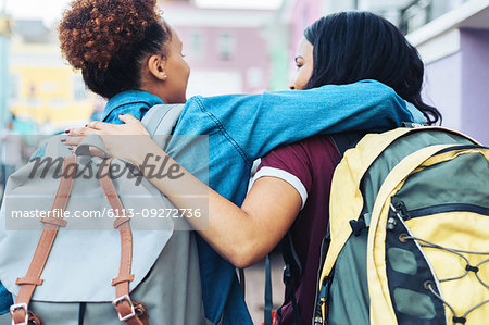 Affectionate young women friends with backpacks hugging