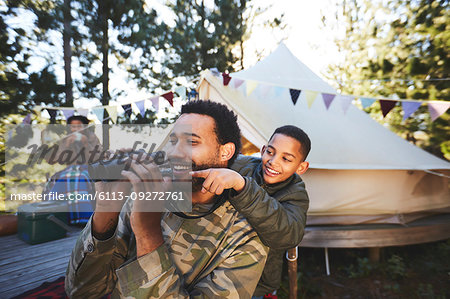 Happy, curious father and son with binoculars at campsite