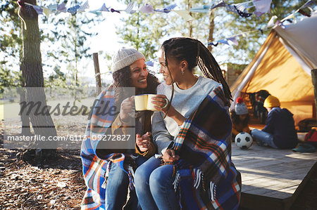 Happy lesbian couple relaxing, drinking coffee at sunny campsite
