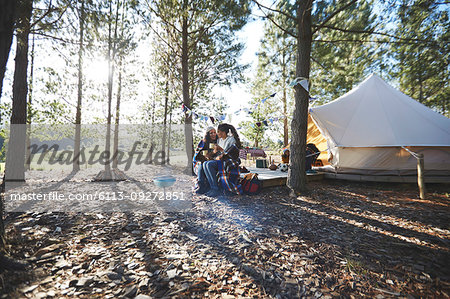 Happy, affectionate lesbian couple relaxing, drinking coffee at sunny campsite in woods