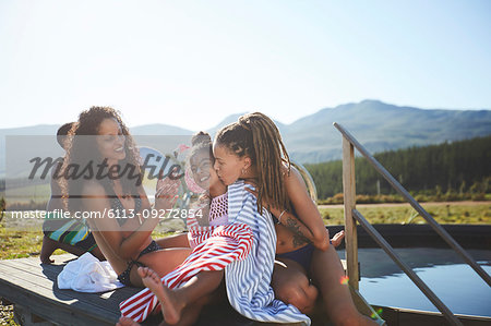 Affectionate lesbian couple and daughter at remote, sunny, summer poolside