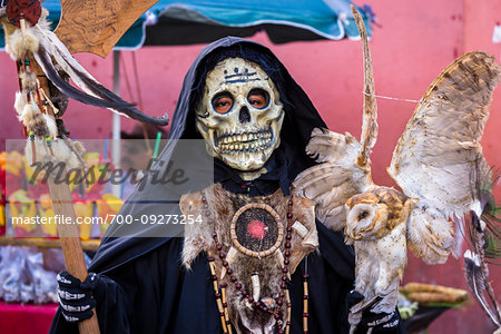 Indigenous tribal dancer wearing grim reaper costume and holding stuffed owl at a St Michael Archangel Festival parade in San Miguel de Allende, Mexico