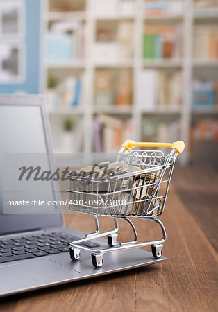 Shopping cart full of money and laptop on a wooden desktop: e-commerce, e-payments and online shopping concept