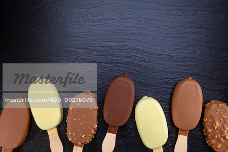 Ice cream on stick covered with chocolate on black stone slate board.