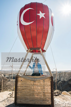 Woman sitting on basket of hot air balloon overlooking fairy chimney valley, Göreme, Cappadocia, Nevsehir, Turkey