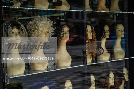 Row of mannequin heads displaying variety of wigs in shop window