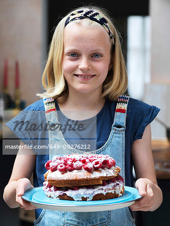 Girl baking a cake, holding homemade cake with raspberries on top in kitchen, portrait
