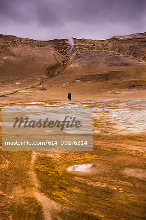 Distant view of two male tourists walking through geothermal landscape, Namaskard hverir, Myvatn, Iceland Distant view of two male tourists walking through geothermal landscape, Namaskard hverir, Myvatn, Iceland