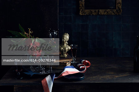 A Bastille Day celebration, tray of glasses with red wine, traditional old master painting and a red white and blue ribbon, colours of the French flag. .